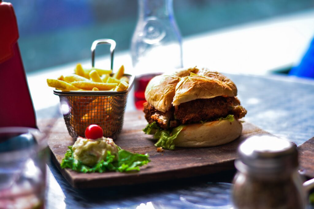 Burger Menü Ein Burger angerichtet auf einem Holzbrett mit Pommes Frites und einer Sauce
